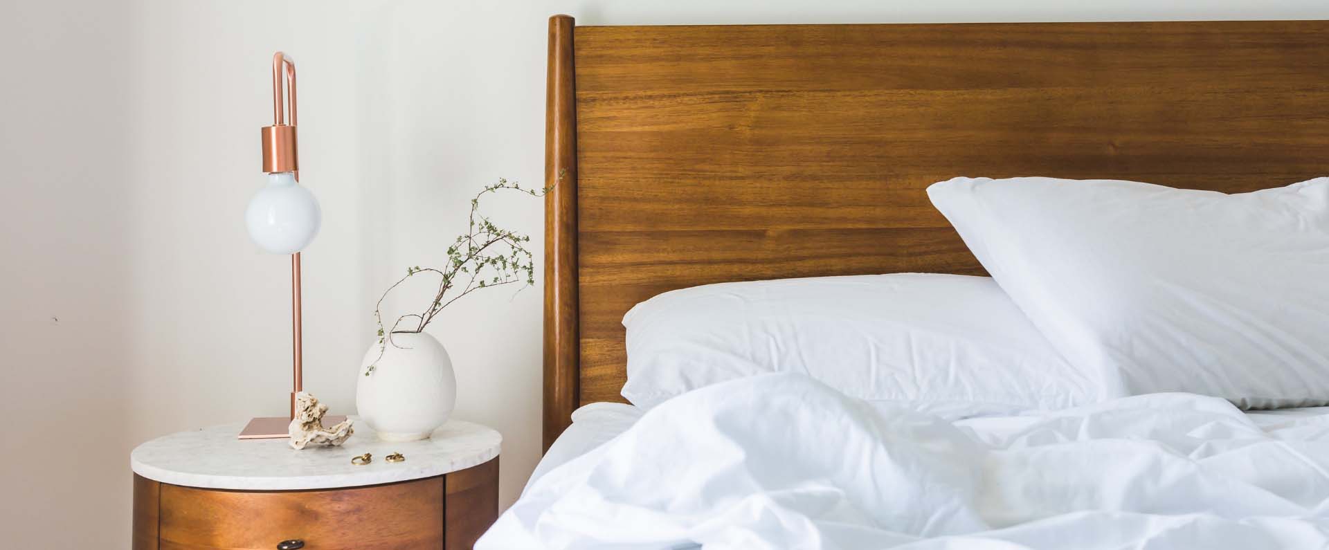 Bed with white sheets, a white lamp and wooden headboard