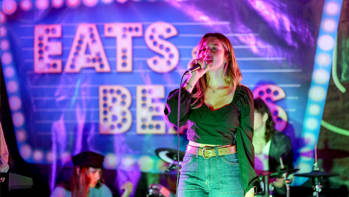 A singer performing in front of Eats and Beats sign